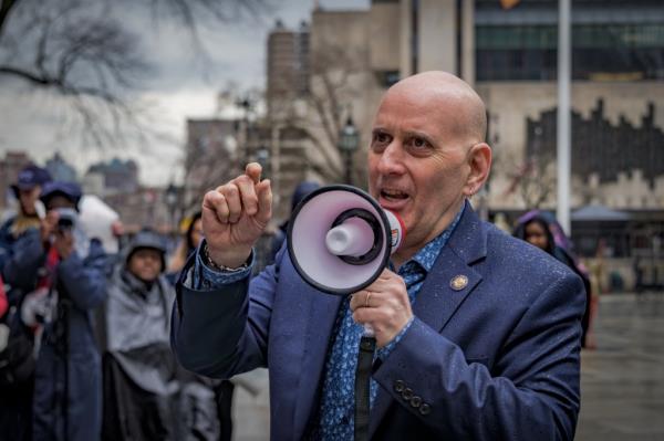 New York State Representative Harvey Epstein speaking into a megaphone at a rally outside City Hall, advocating for investment in the City University of New York
