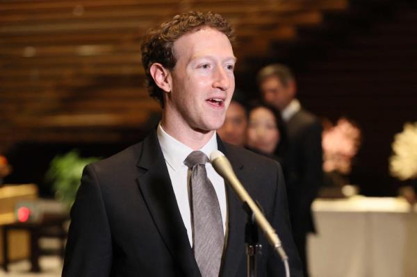facebook ceo mark zuckerburg in a dark suit and grey tie speaks into a microphone