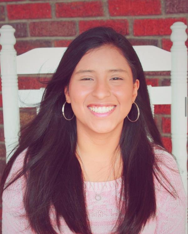 Miriam Arena has long, dark hair, wears a pink sweater and smiles