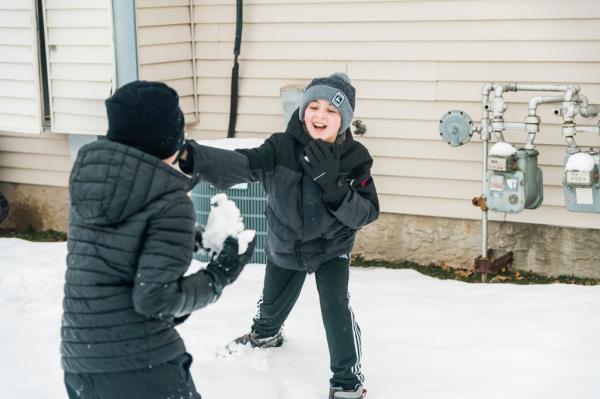Deana Balahtsis-Thomas and her two sons in winter jackets and snow boots outside in the snow.