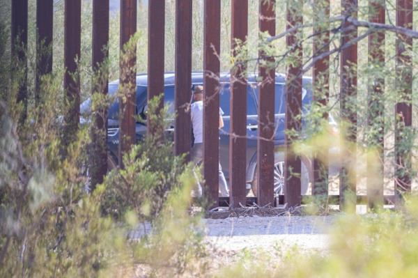 A smuggler in a dark-colored van pulls up the US border wall to dro<em></em>p off illegal immigrants.