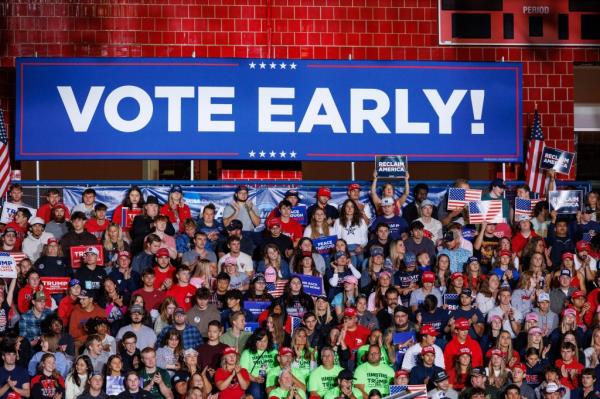 Supporters of former President Do<em></em>nald Trump stand under a banner encouraging them to vote early during a rally in Saginaw, Mich., on Oct. 3, 2024
