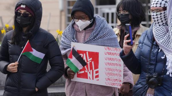 Bilal Hassani, wearing a Palestinian scarf over her shoulders and holding a   pro-Palestinian sign, stands among a group of students protesting at Rutgers University.
