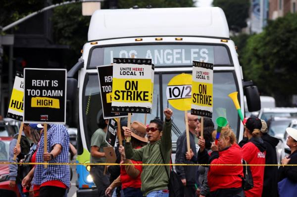 Hotel workers holding signs as they march and protest for their rights in Los Angeles, while a bus driver waits to cross the road, captured on October 25, 2023.