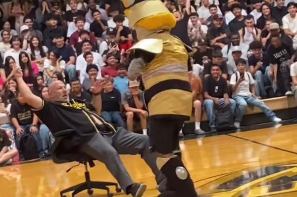 Image of a mascot dancing with a man in a chair at a school rally.