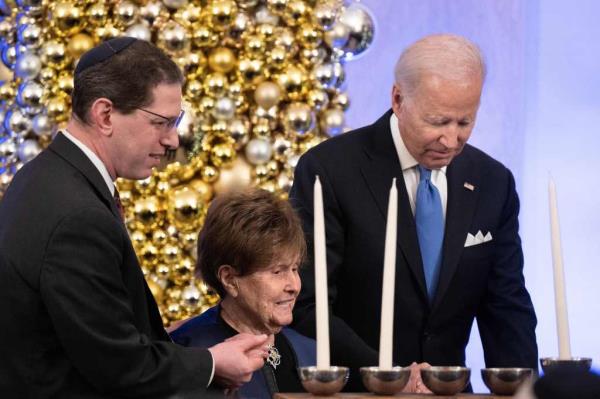 Biden lighting a menorah with Holocaust survivor Bro<em></em>nia Brandman at a 2022 ceremony in the White House on Dec. 19, 2022.