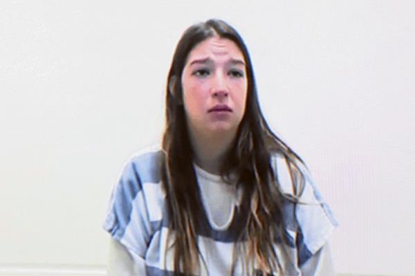 A white woman with long brown hair and a troubled face stands in a blue and white striped prison shirt.
