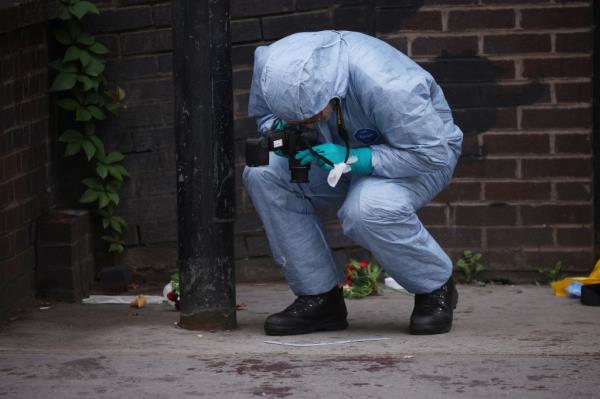 Police forensic officer takes photographs of what looks to be bloodstains at the stabbing scene in Croydon 