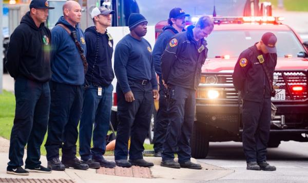 Members of the Austin Fire Department bow their heads as they prepare to drive in a procession leaving Dell Seton Medical Center in Downtown Austin.