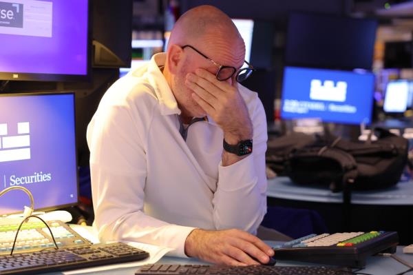 Traders working on the floor of the New York Stock Exchange during a significant market sell-off, with one man covering his face in distress
