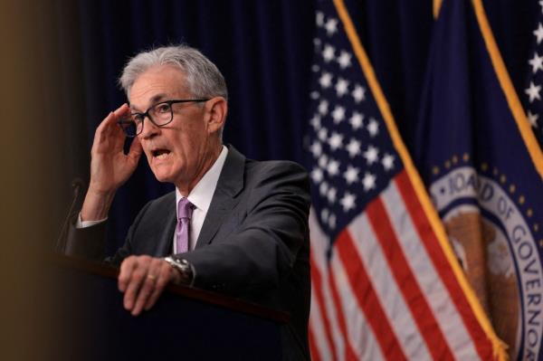 U.S. Federal Reserve Chair Jerome Powell speaking at a press co<em></em>nference a<em></em>bout interest rate policy, with a flag in the background.