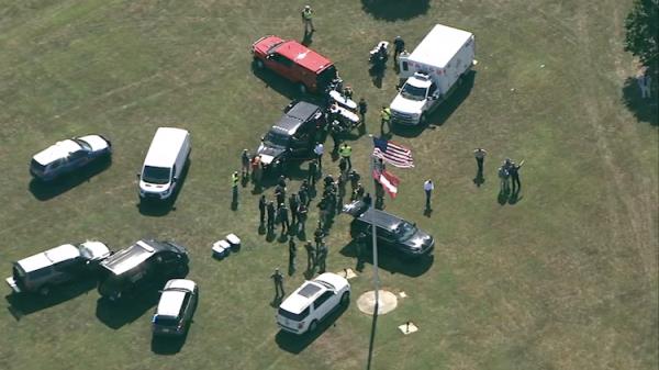 Emergency scene outside Apalachee High School in Winder, Georgia, with a group of people standing around a car after a school shooting incident.