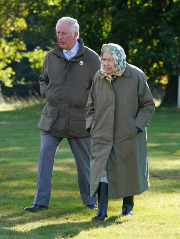 Queen Elizabeth walking on grass with her son, King Charles. 