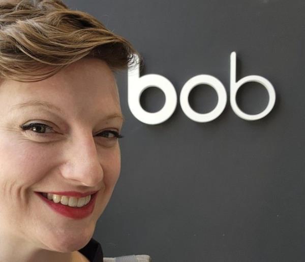Sarah Reynolds in selfie next to sign reading 'bob'. She has short red hair and is wearing red lipstick