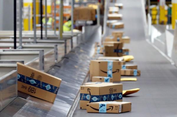 Amazon packages move along co<em></em>nveyer belt at warehouse.