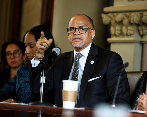 Schools Chancellor David C. Banks speaking at a press conference, pointing and looking out of f<em></em>rame, sitting at dais with other officials.