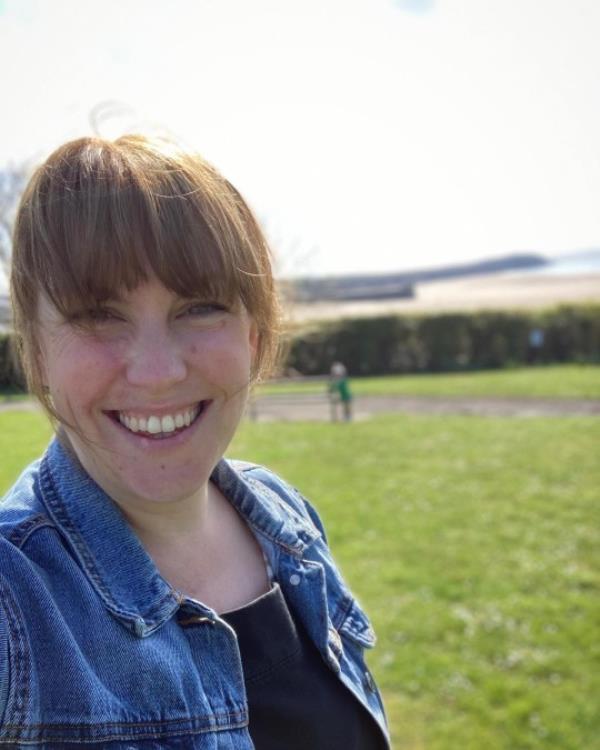 Michelle Morgan Davies outdoors, standing on grass with a beach in the background.