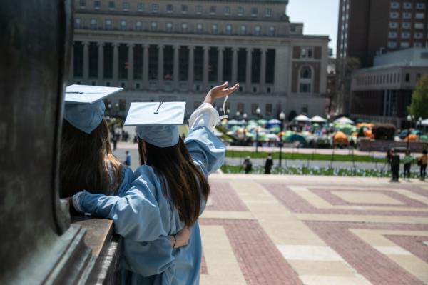 A group of students in blue graduation gowns posing for photos amidst an anti-Israel demo<em></em>nstration at the Gaza Solidarity Encampment at Columbia University