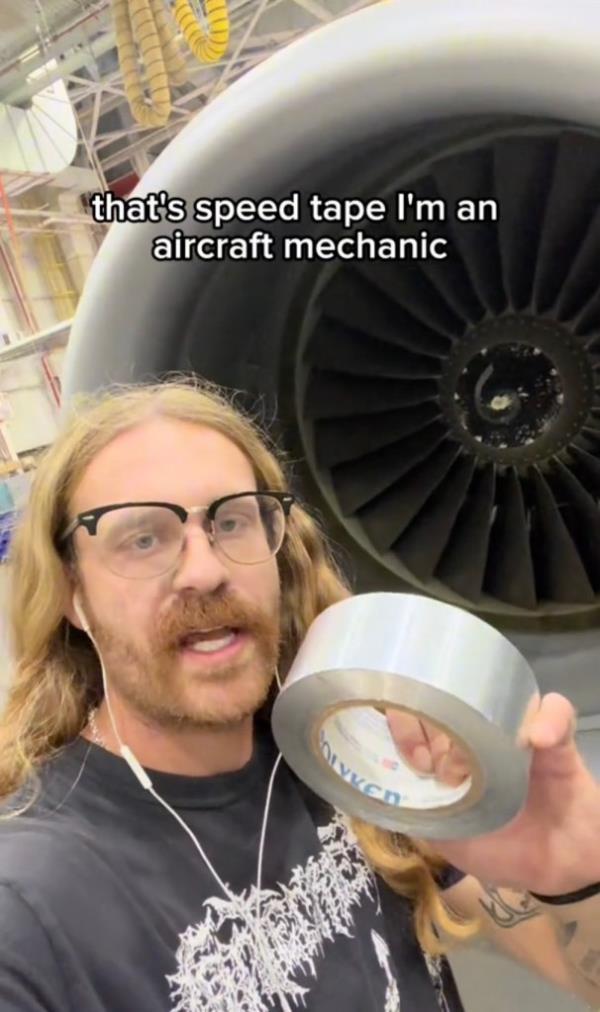 A man with a beard and long hair holds up a roll of silver tape.