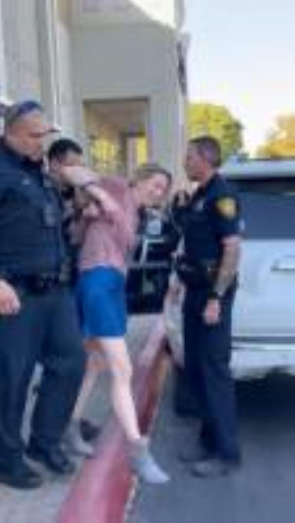 She then is seen being taken out of the business in cuffs by officers, smiling bizarrely and repeating, 