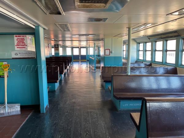 Inside of the ferry with empty benches and windows lining the wall.