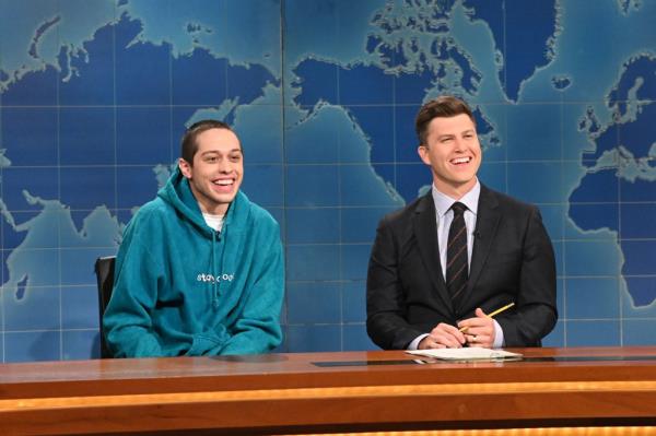 Pete Davidson and Colin Jost smile as they sit behind the 