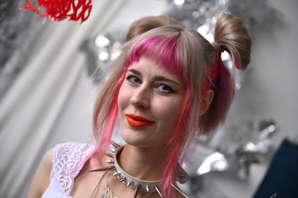 Julia Sinelnikova with pink hair and a spiked necklace standing in her studio.