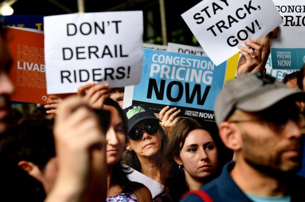 Local leaders and supporters protesting outside NY Governor Kathy Hochul's office against the delay in Co<em></em>ngestion Pricing implementation, holding signs in disagreement