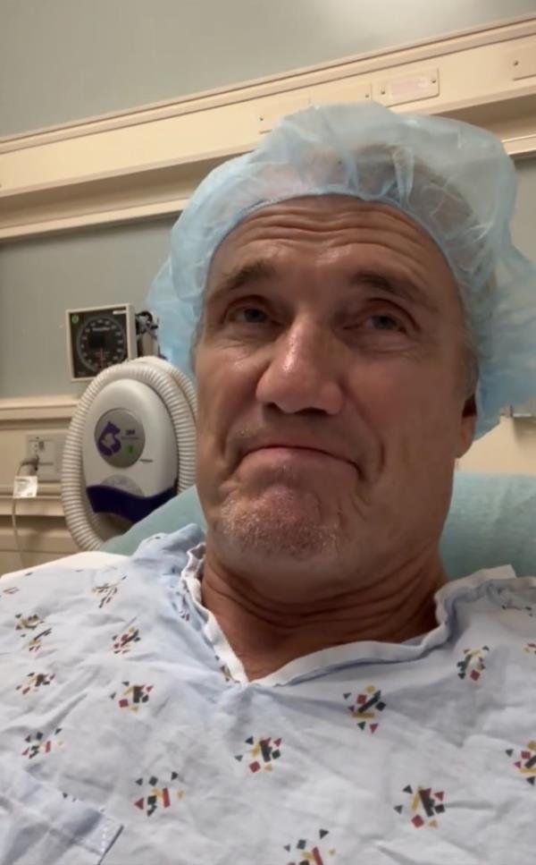 Dolph Lundgren smiling in a hospital bed, celebrating being cancer free after a 9-year battle