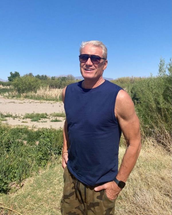 Dolph Lundgren wearing sunglasses and a tank top, standing in a field, revealing his 8-year cancer battle