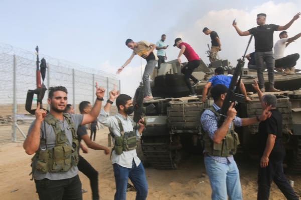 Men standing on an Israeli tank at the Gaza Strip border, celebrating while surrounded by smoke and debris.