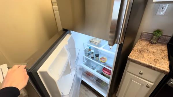 A minimalist woman named Alicia Rice living in an expensive city, San Diego, with her refrigerator door open showcasing minimal food items, substantiating her low-cost lifestyle.