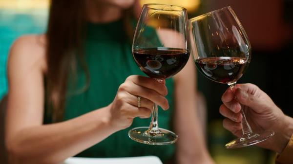 Cropped image of couple cl<em></em>inking glasses of red wine when havin<em></em>g romantic date in restaurant